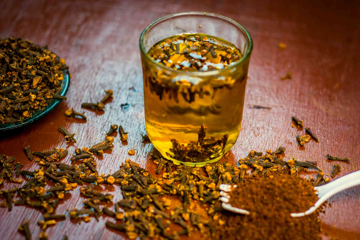 Cloves sit on a table next to ground cloves and a glass full of cloves