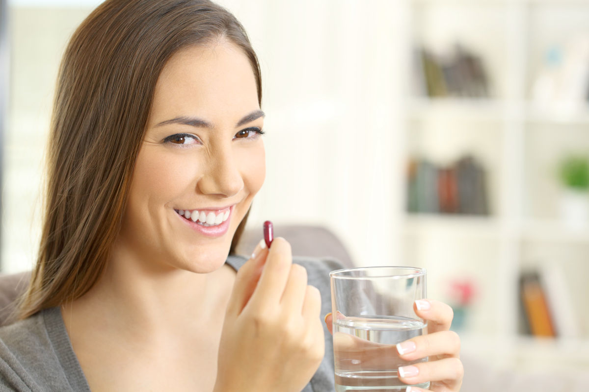 Happy woman looking at camera holding a pill and a glass of water | Natural Brain Vitamins To Improve Your Memory And Focus