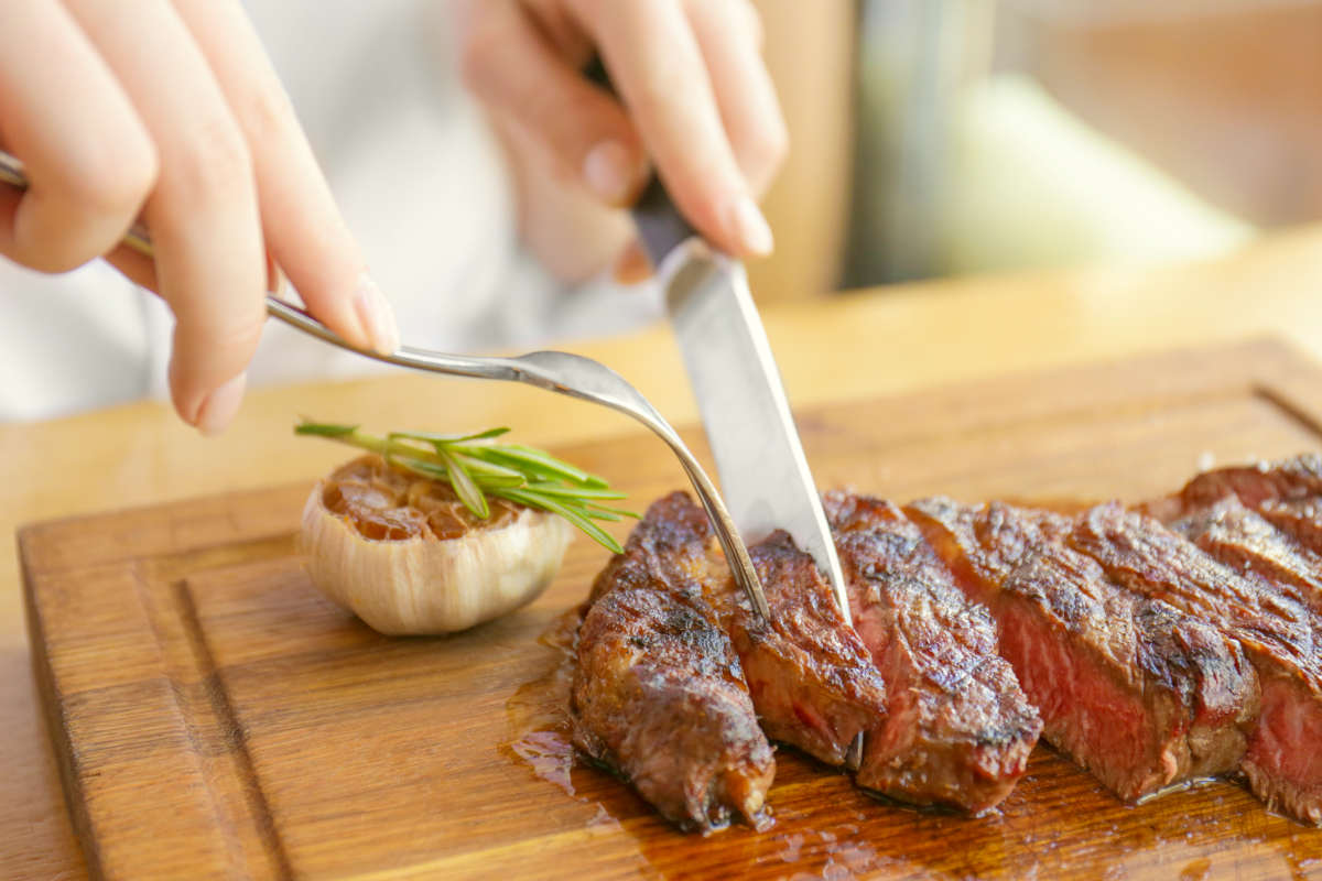 Young woman eating grilled steak in restaurant | Risks Of High TMAO And How To Reduce TMAO Levels