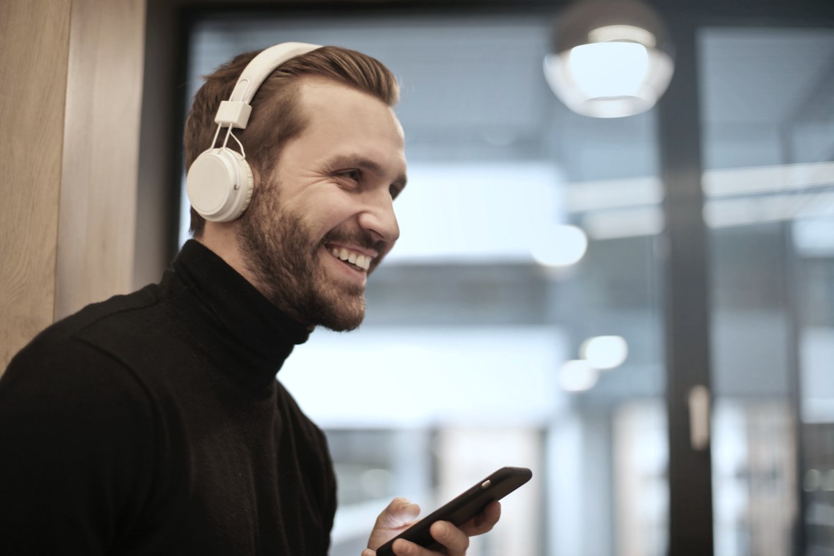 man happily listening to music wearing white headphones inside office | Reasons Why Listening To Peaceful Music Is Good For Your Health peaceful sleep music
